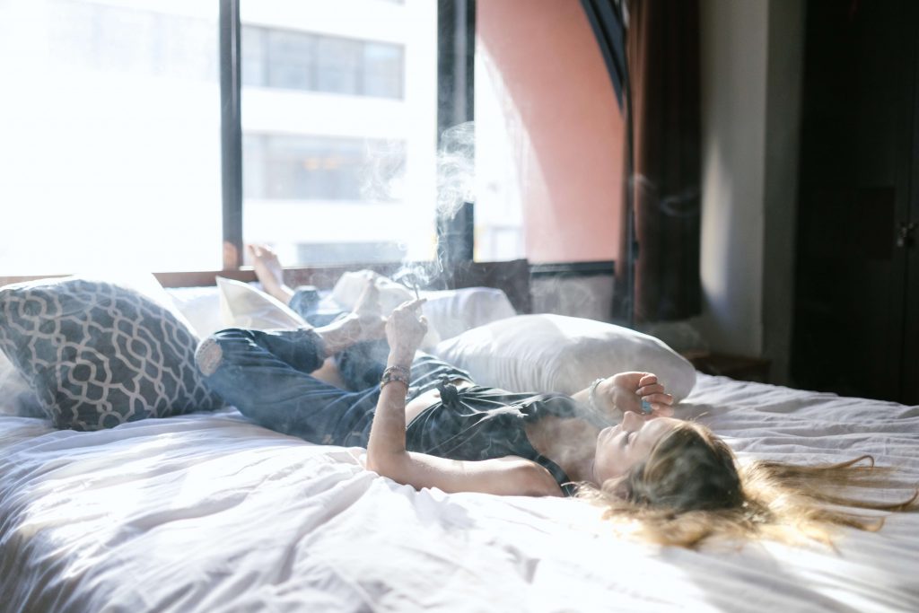 woman laying on back in bed with blonde hair smoking weed joint trying to cure hangover